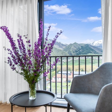 Ein eleganter Raum mit einem blauen Sessel, einem Tisch und einer Vase voller lila Blumen, die auf die Berge blicken.
