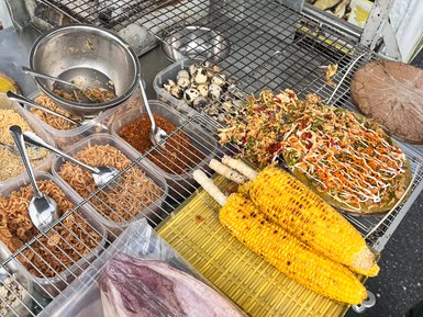 Ein Straßenstand in Vietnam bietet eine Vielzahl von köstlichen Speisen, darunter gegrillte Würstchen und frisches Gemüse.