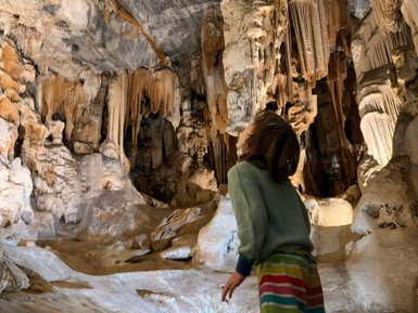 Ein Kind steht in einer beeindruckenden Höhle, umgeben von faszinierenden Stalaktiten und Stalagmiten.