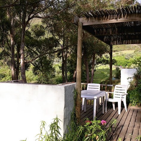 Eine gemütliche Terrasse mit weißen Stühlen und Tisch, umgeben von üppigem Grün und hohen Eukalyptusbäumen.