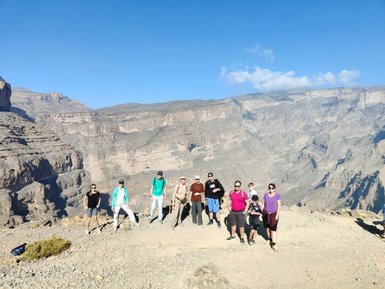 Reisende posieren gemeinsam vor der beeindruckenden Bergkulisse des Jebel Shams für ein Erinnerungsfoto – Oman Reise mit Kindern