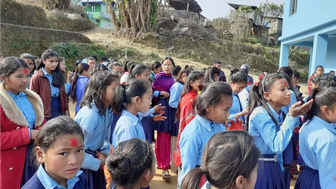 Eine Gruppe von Schülerinnen in blauen Uniformen versammelt sich auf einem Schulgelände, einige tragen rote und bunte Kleidung.