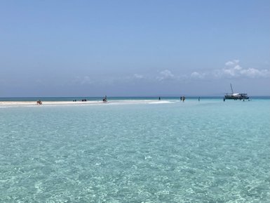 Eine Gruppe von Menschen genießt den sonnigen Tag an einem weißen Sandstrand, umgeben von klarem, türkisfarbenem Wasser.