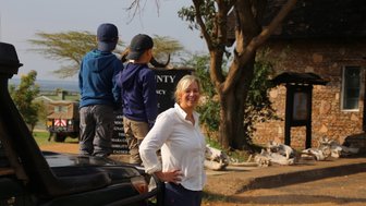 Eine Frau lächelt vor einem Schild, während zwei Kinder auf einem Geländewagen stehen und die Umgebung erkunden.