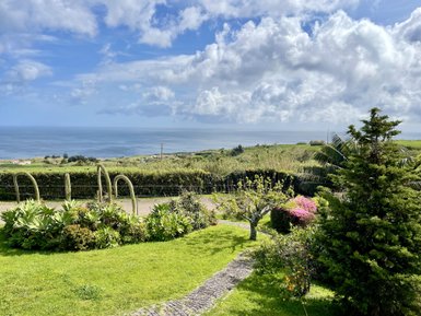 Eine grüne Gartenlandschaft mit bunten Blumen und Blick auf das ruhige Meer unter einem bewölkten Himmel.