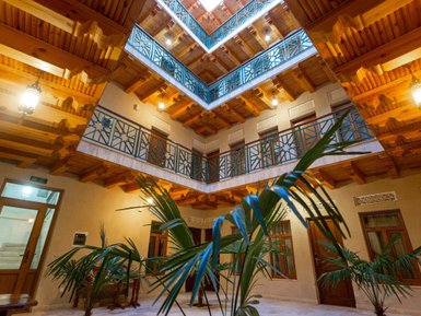 Ein einladender Innenhof mit Holzdecke und kunstvollen Geländern, umgeben von grünen Pflanzen und warmem Licht.