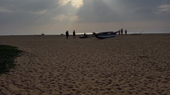 Am Strand von Negombo stehen Menschen vor einem dramatischen Himmel, während die Sonne durch die Wolken strahlt.