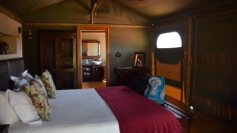 Ein gemütliches Zimmer mit einem großen Bett, dekoriert mit bunten Kissen und einem roten Überwurf, strahlt Ruhe aus.