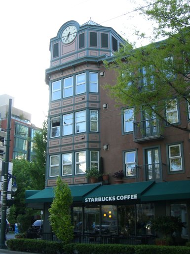 Ein elegantes Gebäude mit einer großen Uhr auf dem Dach und einem Starbucks-Café im Erdgeschoss, umgeben von Bäumen.