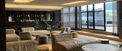 Ein eleganter Lobbybereich mit bequemen, hellen Sofas und einem stilvollen Tisch, umgeben von großen Fenstern.