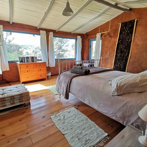 Ein gemütliches Schlafzimmer mit einem großen Bett, Holzfußboden und einem Fenster, das auf eine grüne Landschaft blickt.