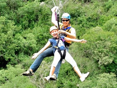 Fröhliches Kind beim Ziplining über Baumwipfel in einem Abenteuerpark in Südafrika – Südafrika Reise mit Kindern
