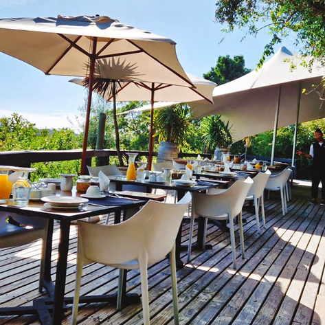Ein einladender Außenbereich eines Restaurants mit gedeckten Tischen und Sonnenschirmen, umgeben von üppigem Grün.