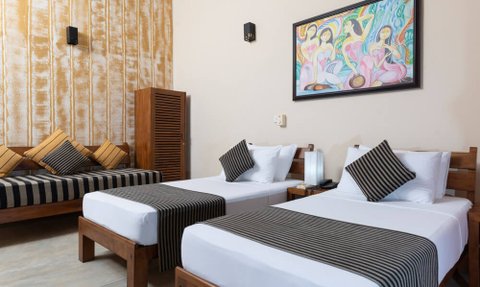 Ein helles Zimmer mit zwei Einzelbetten, gestreiften Bettüberwürfen und einem gemütlichen Sofa mit Kissen im Hintergrund.