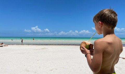 Junge genießt Kokoswasser direkt aus der Frucht am Strand von Puerto Morelos – Mexiko Familienreise