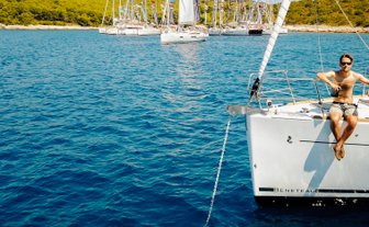 Ein junger Mann sitzt entspannt auf der Reling einer Segelyacht und genießt die Sonne auf dem blauen Wasser.