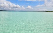 Ein klarer, türkisfarbener Ozean erstreckt sich unter einem strahlend blauen Himmel mit weißen Wolken.