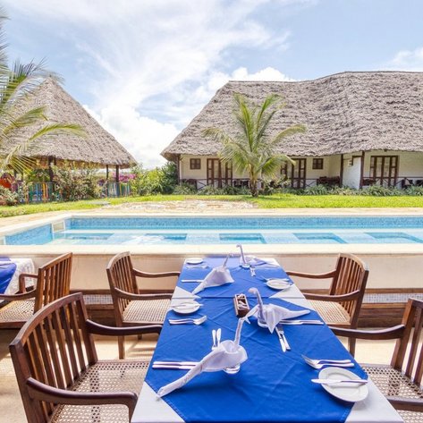 Ein eleganter Restaurantbereich mit blauen Tischdecken, umgeben von Palmen und einem glitzernden Pool im Hintergrund.
