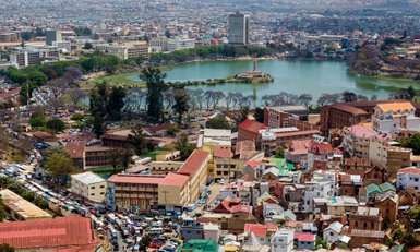 Ein Blick auf Antananarivo mit bunten Gebäuden und einem ruhigen See, umgeben von grünen Bäumen und blühenden Pflanzen.