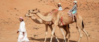 Beduine führt zwei Kamele mit zwei Mädchen durch die Wüste – Oman Familienreise