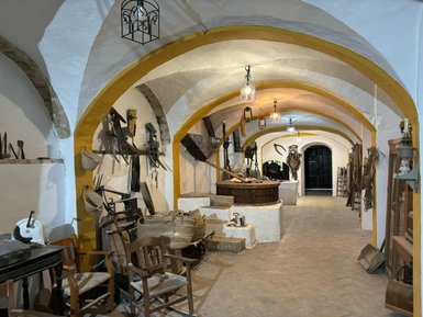 Ein historischer Raum mit gewölbten Decken, der mit landwirtschaftlichen Werkzeugen und Möbeln dekoriert ist.