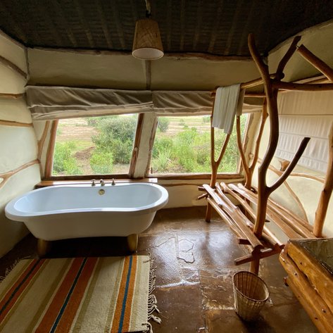 Ein stilvolles Badezimmer mit einer freistehenden Badewanne und einem rustikalen Holzregal, umgeben von großen Fenstern.