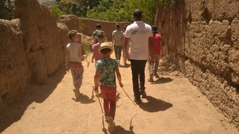 Eine Gruppe von Kindern und einem Erwachsenen wandert durch einen schmalen, sonnigen Pfad in einer Oase.