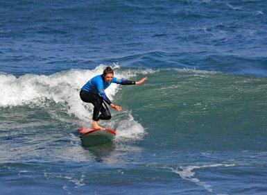 Eine Surferin in einem blauen Neoprenanzug reitet auf einer Welle und zeigt Geschicklichkeit und Balance.