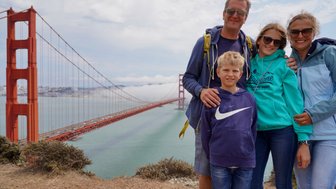 Eine Familie posiert fröhlich vor der Golden Gate Bridge, umgeben von einer malerischen Küstenlandschaft und leichtem Nebel.