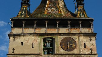 Der Turm mit bunten Schindeln und einer großen Uhr zeigt eine historische Architektur unter blauem Himmel.