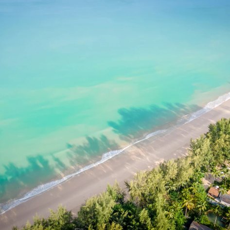 Ein atemberaubender Blick auf den ruhigen Strand mit klarem, türkisfarbenem Wasser und sanften Wellen, umgeben von üppigem Grün.