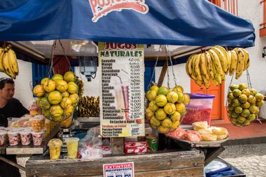 Ein Marktstand in Medellín bietet eine Vielzahl frischer Früchte und Säfte an, darunter Bananen und Orangen in Netzen.
