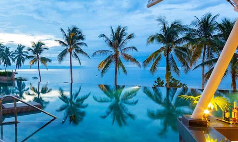 Ein stilvoller Pool am Strand, umgeben von Palmen, spiegelt sanft den Himmel während der Dämmerung wider.
