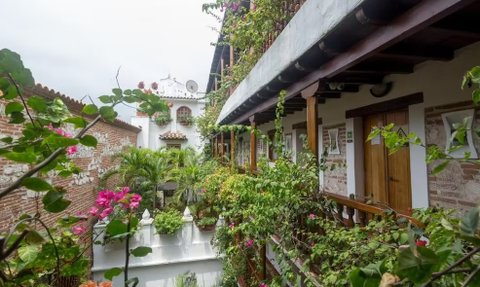 Ein malerischer Innenhof in Cartagena, umgeben von üppigem Grün und bunten Blumen, mit traditionellen Kolonialgebäuden im Hintergrund.