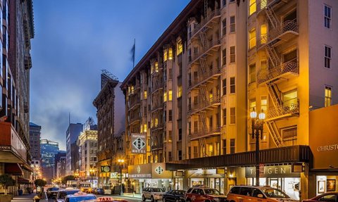 Die belebte Straße in San Francisco zeigt das Handlery Hotel mit leuchtenden Fenstern und Taxis, die am Abend parken.
