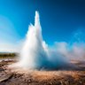 Ein beeindruckender Geysir sprudelt in die Höhe, umgeben von dampfenden Quellen und einer klaren blauen Himmel.