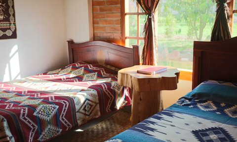 Ein gemütliches Zimmer mit zwei Betten, die mit bunten Decken bedeckt sind, und einem rustikalen Holztisch in der Mitte.