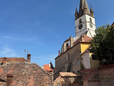 Die malerische Altstadt von Sibiu mit roten Ziegeldächern und einer beeindruckenden Kirchturmspitze unter blauem Himmel.