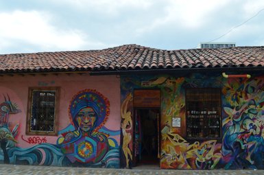 Bunte Wandmalereien zieren die Fassade eines Hauses in Bogotá, mit einem auffälligen Porträt einer Frau im Vordergrund.