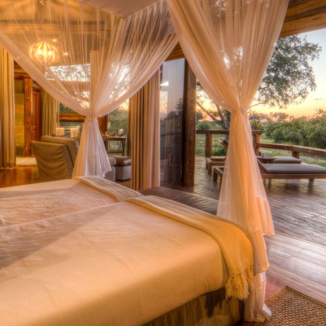 Ein elegantes Schlafzimmer mit zwei Betten, umgeben von Moskitonetzen, bietet einen Blick auf die Natur bei Sonnenuntergang.