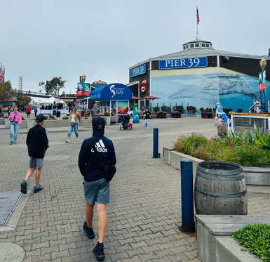 Zwei Kinder gehen in Richtung Pier 39, umgeben von Menschen und bunten Geschäften in einer lebhaften Küstenatmosphäre.