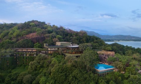 Ein modernes Hotelgebäude schmiegt sich an einen bewaldeten Hang, umgeben von üppigem Grün und sanften Hügeln.
