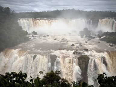 Der mächtige Wasserfall ergießt sich über die Klippen, umgeben von üppigem grünem Gelände und mistigen Nebelschwaden.
