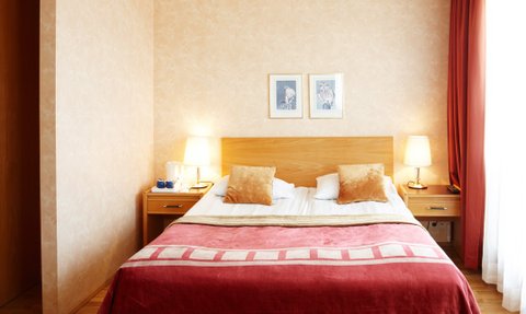 Ein gemütliches Schlafzimmer mit einem großen Bett, dekoriert mit Kissen und einer roten Decke, umgeben von warmem Licht.