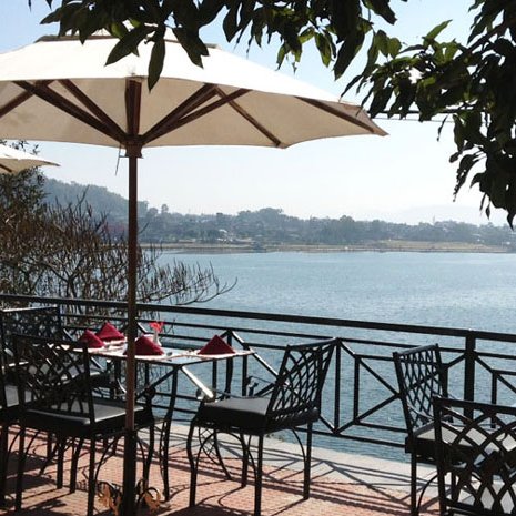 Ein malerischer Blick auf einen ruhigen See, umgeben von Bäumen und einem einladenden Restaurantbereich mit Sonnenschirmen.