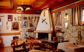 Ein rustikales Restaurant mit Holzmöbeln, einem offenen Kamin und dekorativen Werkzeugen an den Wänden.
