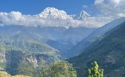 Majestätische schneebedeckte Berge erheben sich über grüne Täler, während Wolken sanft darüber ziehen und die Landschaft umhüllen.