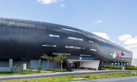 Ein modernes, schwarzes Gebäude mit großen Fenstern und dem Schriftzug 'Wyndham' an der Fassade, umgeben von Grünflächen.