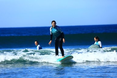 Ein Surfer steht auf seinem Brett und balanciert geschickt auf den Wellen, während andere Surfer im Hintergrund paddeln.