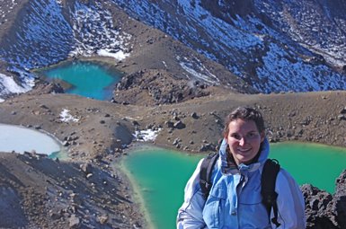 Eine Frau mit einem Rucksack lächelt vor einer beeindruckenden Berglandschaft mit türkisfarbenen Seen.